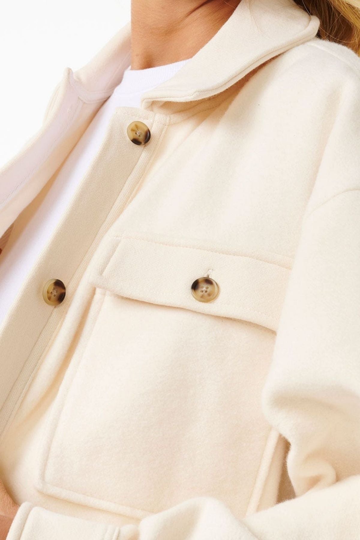 A close-up shows a person in the Rip Curl High Tide Fleece Shacket, featuring large buttons and a chest pocket over a white shirt. The lower face, neck, and upper torso are visible—a stylish pick for adventurous individuals.