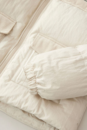 A close-up of the Rip Curl High Tide Mixed Cord Puffer in light beige, showing its zippered front, flap pockets, elasticated sleeve cuff, crinkled-texture fabric, and embroidered logo.