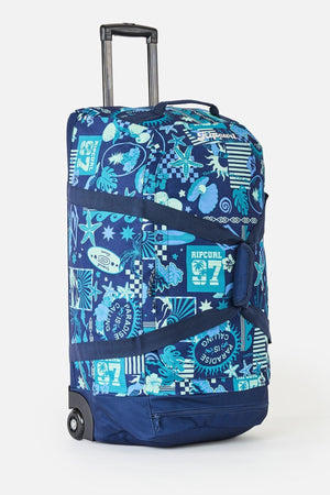 The Rip Curl Jupiter 80L Mixed Travel Bag is blue with surf and sea-themed patterns, a white turquoise logo, retractable handle, two wheels, black straps, and made from durable recycled polyester.