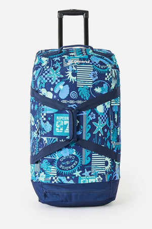 The Rip Curl Jupiter 80L Mixed Travel Bag is a blue luggage made from recycled polyester, featuring a retractable handle, tropical and geometric blue, white, and teal patterns, and the Rip Curl logo on the front.