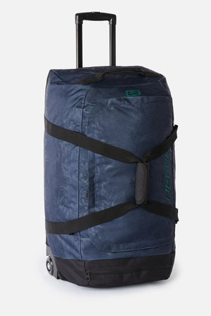 Dark blue patterned Rip Curl Jupiter Archive 80L rolling duffel bag with black straps, a telescoping handle, and wheels.