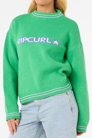 A person sports the Rip Curl Las Dalias Sweater with "RIP CURL" and star logo in white and blue yarn-dyed stripes, paired with light blue jeans. The sweater has ribbed cuffs plus a collar with white and green stripes.