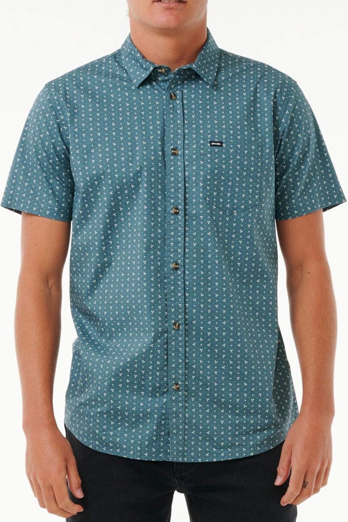A man stands facing forward wearing the Rip Curl Micro Short Sleeve Shirt in teal with a small white geometric print, front pocket, and subtle black tag. The shirt is made from a soft cotton blend; the man’s head is not fully visible.