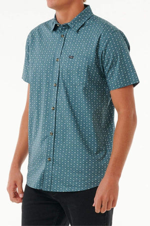 A man wears the Rip Curl Micro Short Sleeve Shirt in teal with a small white geometric print and black pants, standing against a plain white background.