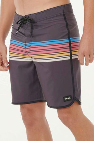 A person wears the Rip Curl Mirage Surf Revival 19" Boardshort, made from recycled PET, in gray with blue, pink, yellow, and orange stripes, a black drawstring, and a small “Rip Curl” logo near the hem. Only the lower torso and legs are shown.