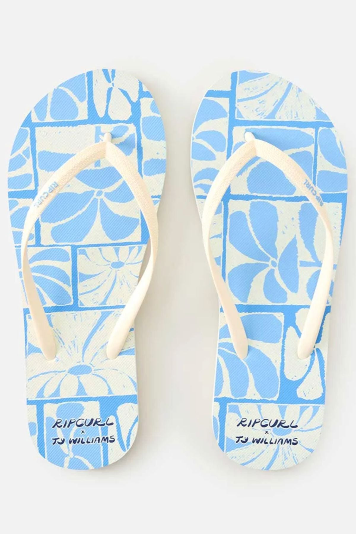 The Rip Curl Mixed Bloom Thongs feature blue footbeds with white straps, a comfy 3-point design, a white floral geometric pattern, and “RIP CURL” plus “TJ WILLIAMS” printed on algae-blended foam EVA footbeds.