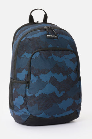 Rip Curl Ozone 30L Camo Check backpack in blue and black, featuring a dark, abstract mountain-like pattern and a front zippered pocket.