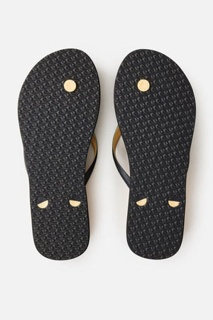 A pair of Rip Curl Premium Surf Bloom Thongs viewed from the bottom. The black soles feature a textured pattern and have visible tan plugs where the straps are attached. The background is a plain white surface.