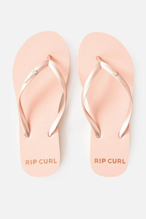 A pair of Rip Curl Premium Surf Bloom Thongs in light pink with matching metallic pink straps, featuring a small decorative button. The brand name "RIP CURL" is printed on the sole of each thong near the heel.
