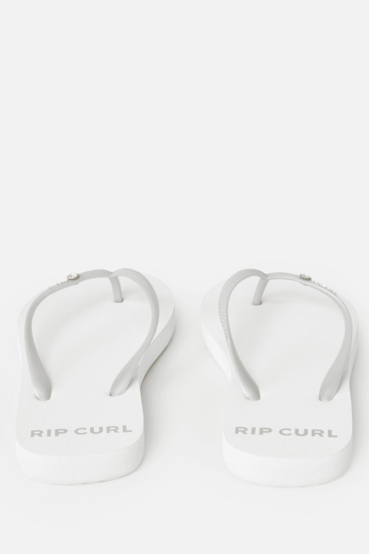 The Rip Curl Premium Surf Bloom Thongs feature a white base with light gray straps and the brand name printed in gray on the heel, making them a stylish beach footwear choice. Displayed on a plain white background.