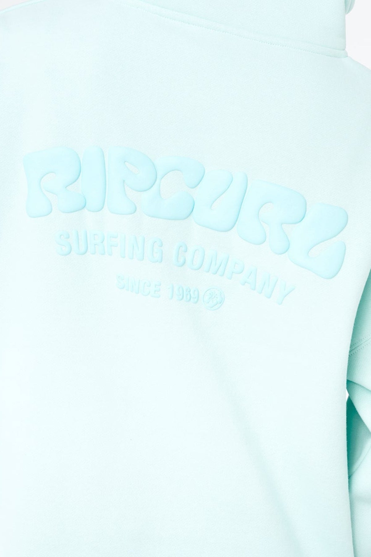 Close-up of a light blue Rip Curl Surf Puff 1/4 Zip hoodie featuring raised "RIP CURL SURFING COMPANY SINCE 1969" text on the back—ideal for a timeless surf-inspired look.
