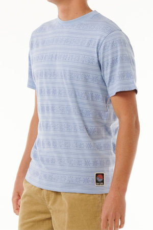 A person wearing the Rip Curl Saltwater Culture Stripey Tee in light blue with jacquard stripes and tan corduroy pants, standing against a plain white background.