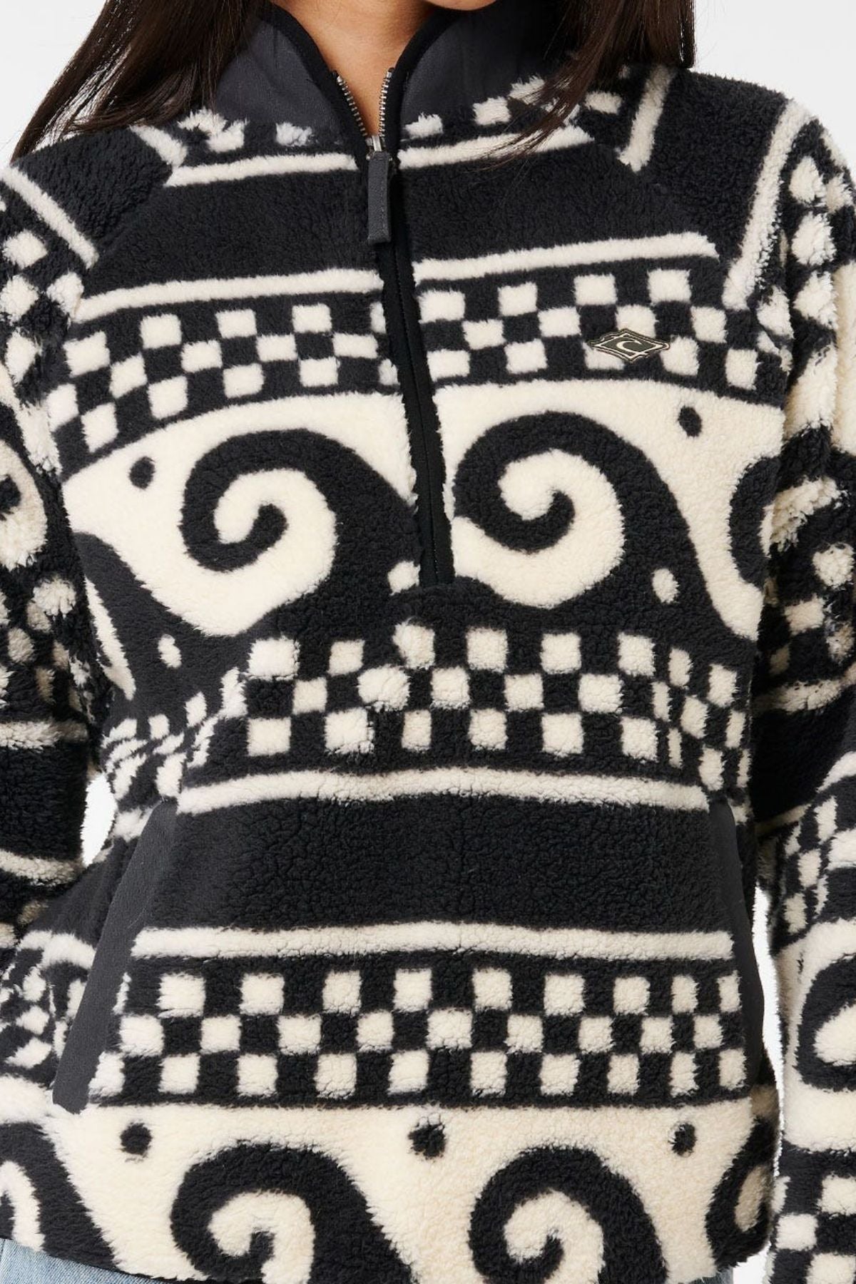 A person wearing the Rip Curl San Carlos Polar Fleece—a fuzzy black and white jacket with swirl and checkerboard patterns, a front zipper, and side pockets. Only the lower face and torso are visible.
