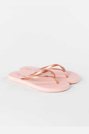 A pair of Rip Curl Script Wave Bloom Thongs in light pink, crafted from eco-friendly materials with slim straps and a slight sheen, showcased against a white background.