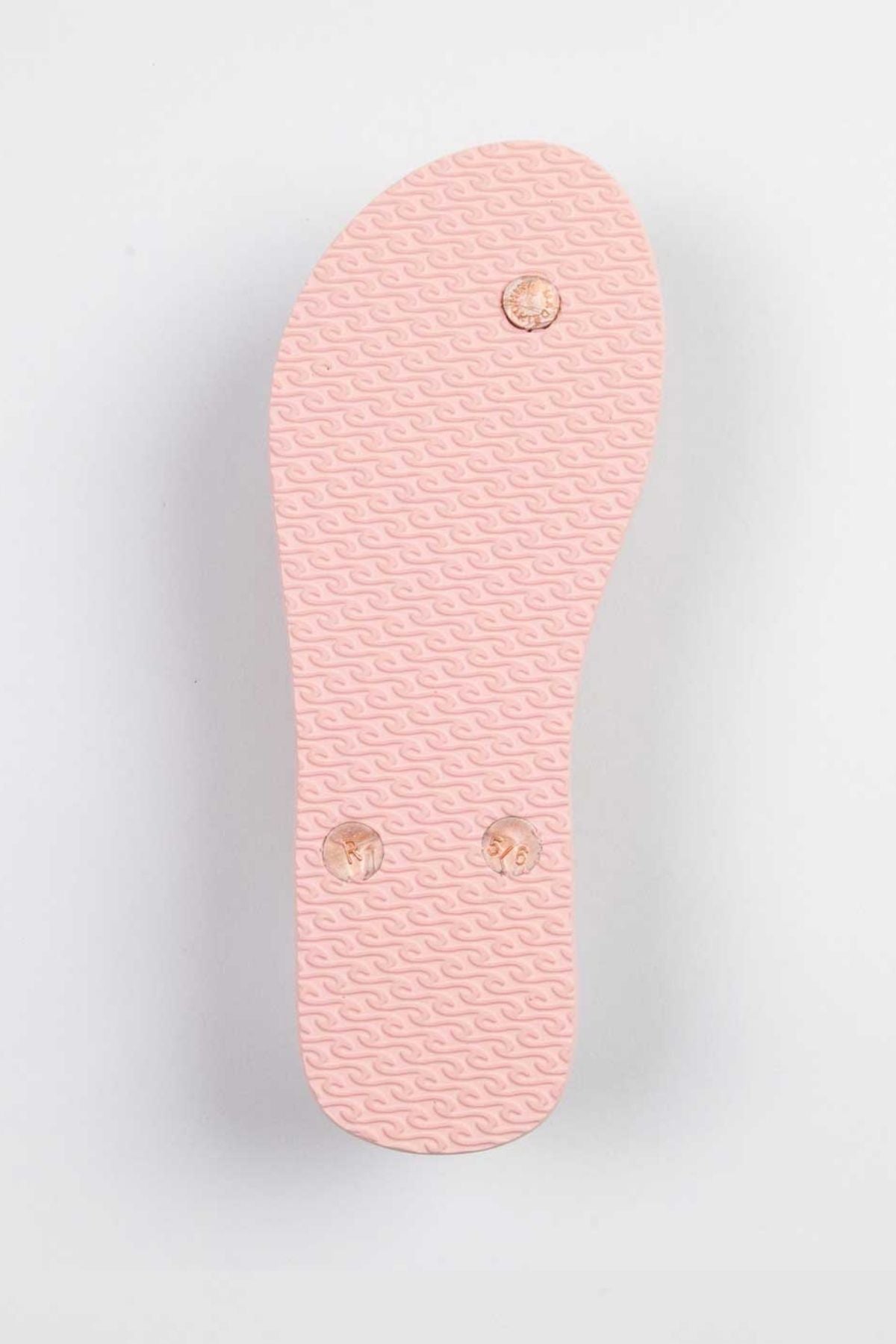 The image displays the underside of a Rip Curl Script Wave Bloom Thong in pink, showcasing a textured wave pattern. Made from eco-friendly materials, it includes two round plugs and one visible screw on its surface.