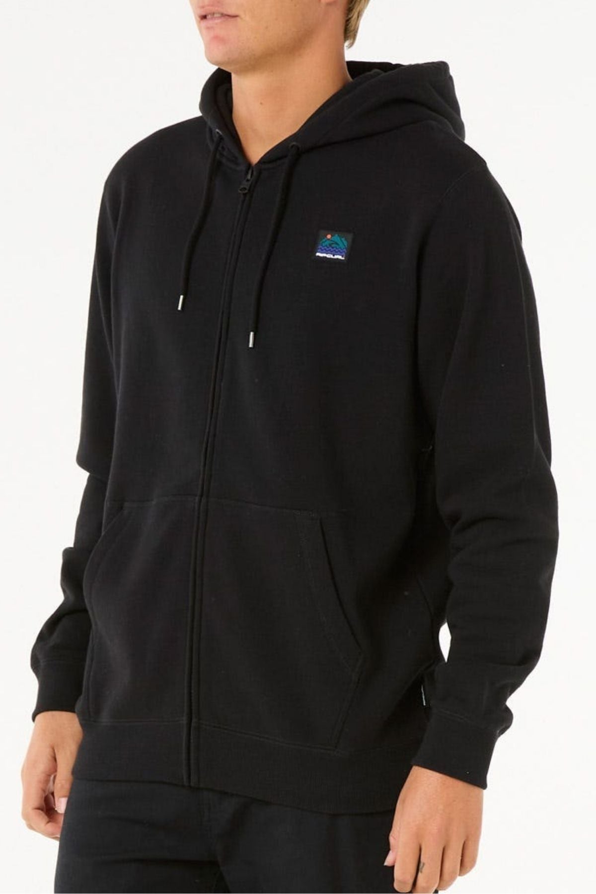 A person wears a Rip Curl Search Zip Thru Hood—a standard fit cotton-poly hoodie with drawstrings, front pockets, and a small colorful rectangular patch on the left chest—standing against a white background.