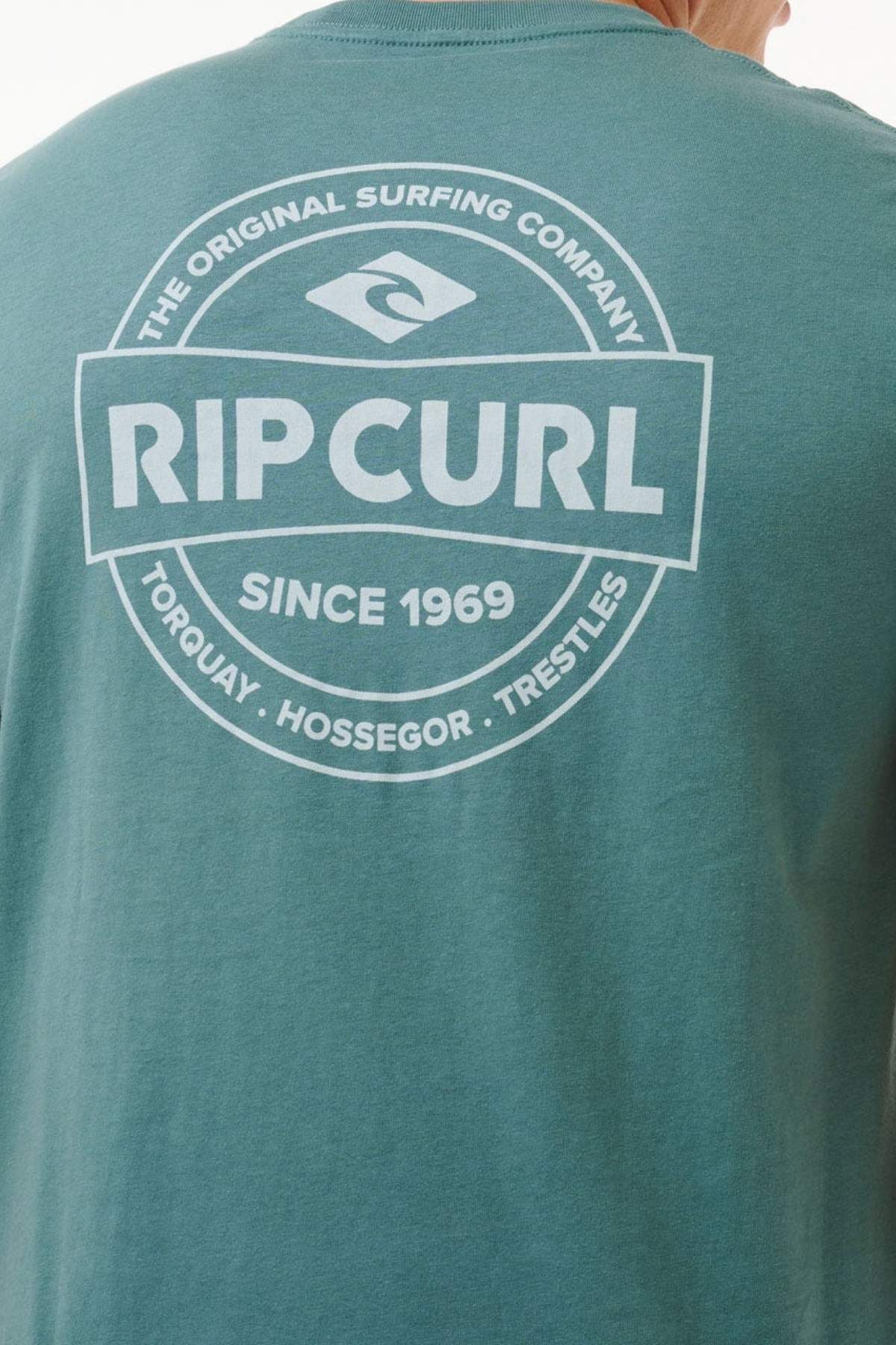 The back of the Rip Curl Staple Tee features a striking white "RIP CURL" logo with "THE ORIGINAL SURFING COMPANY," "SINCE 1969," and Torquay, Hossegor, Trestles encircling the design on teal cotton jersey.