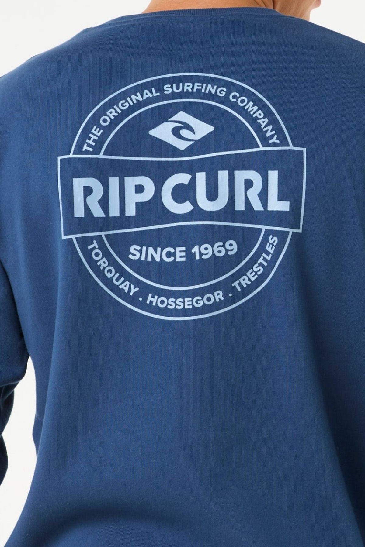 The Rip Curl Stapler Crew sweatshirt is made from cotton-polyester fleece in blue, with unique front and back prints featuring a large white circular logo that says "Rip Curl," "Since 1969," and iconic surf spots.