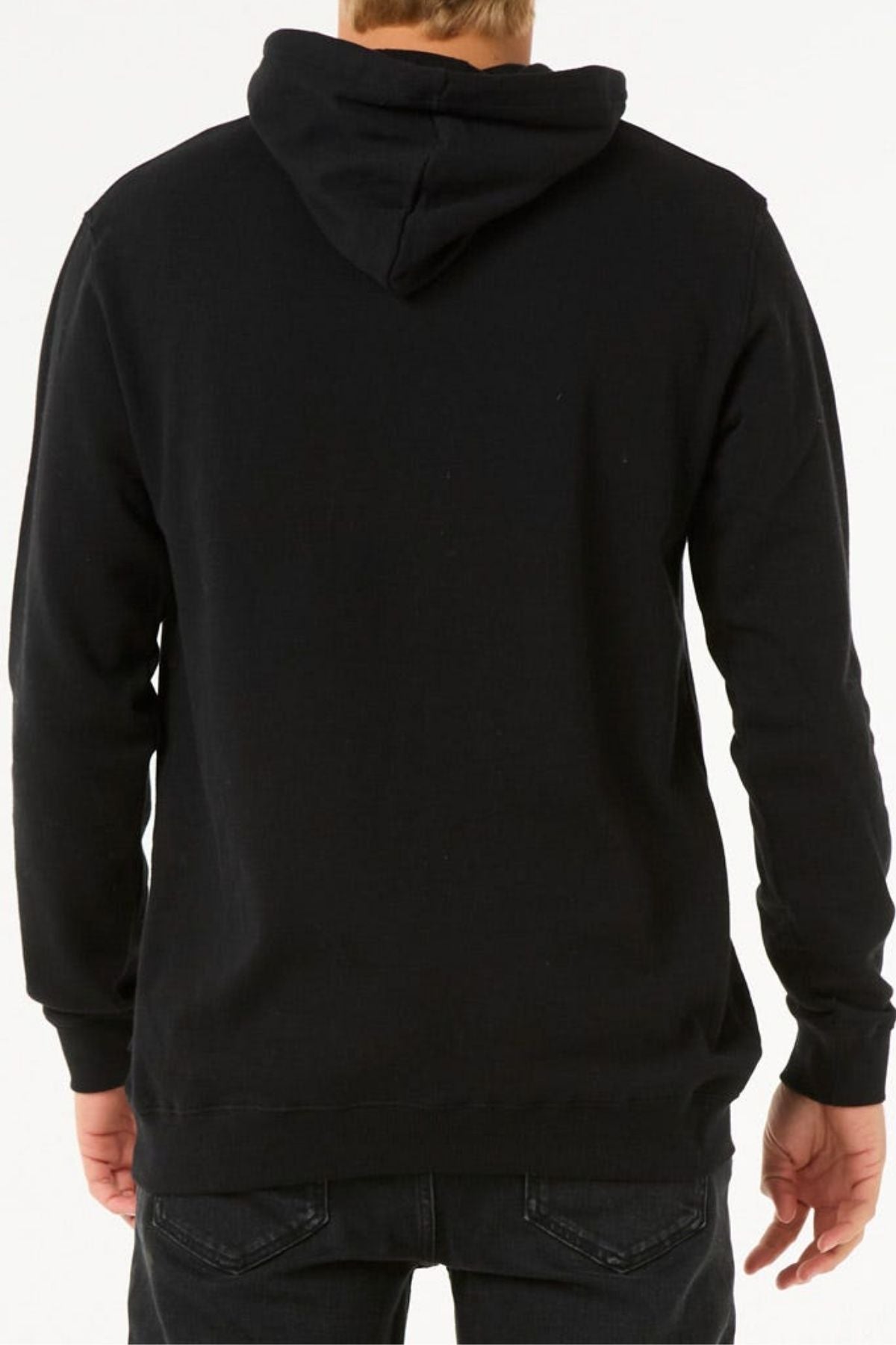 Someone is standing with their back to the camera against a plain light background, wearing the Rip Curl Stapler Hood black cotton-polyester fleece hoodie and black jeans.