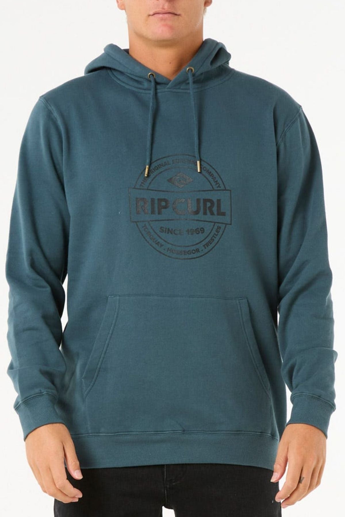 A person wears the Rip Curl Stapler Hood in teal, made from soft cotton-polyester fleece. It features a front pocket, drawstrings, and the black Rip Curl logo with "Since 1969" on the chest. Shown from shoulders to hips.