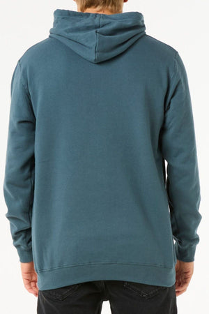 Someone is seen from the back against a white background wearing a teal Rip Curl Stapler Hood hoodie, made from cotton and polyester fleece, with black pants. The hood is up but not covering their head.