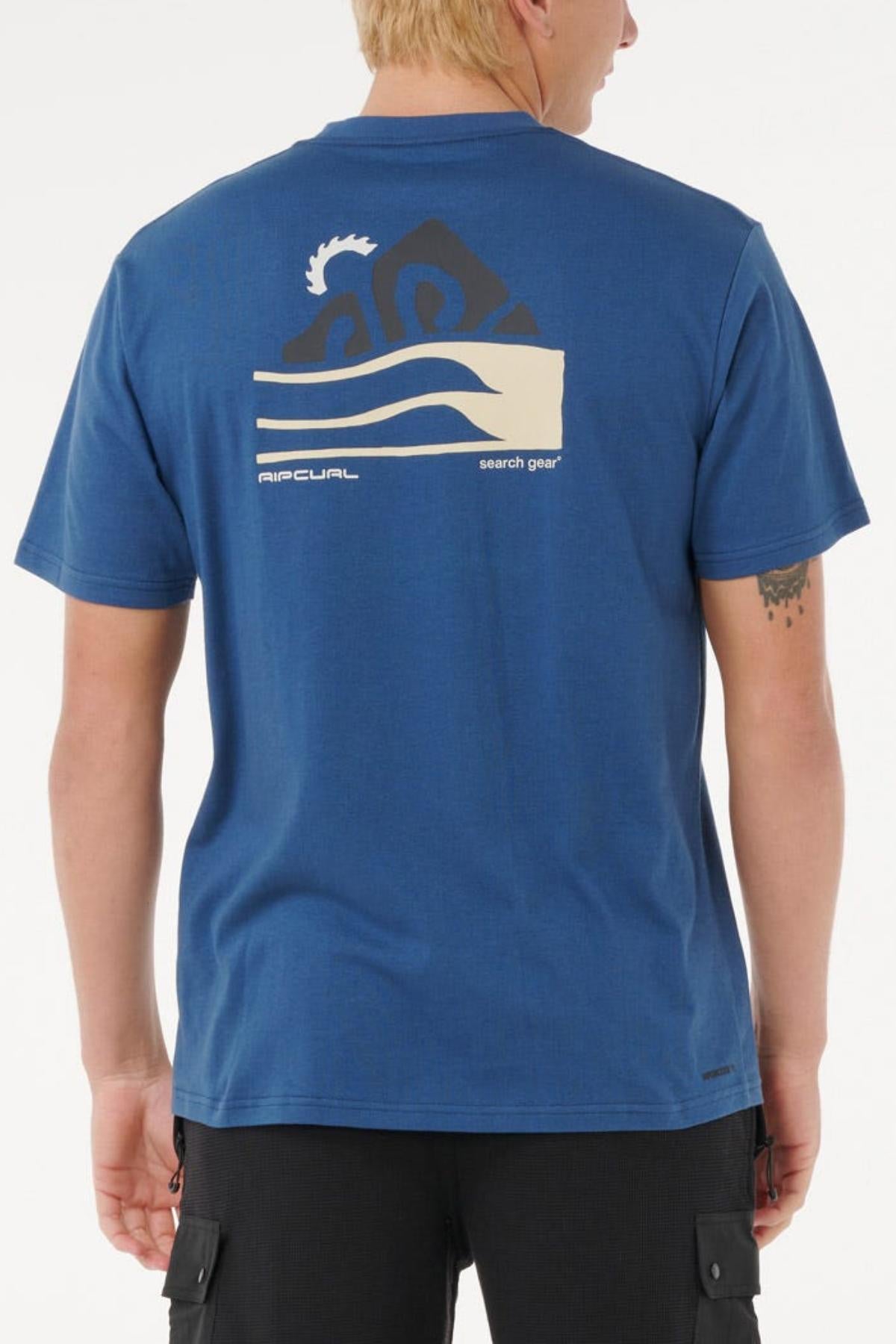 A person with short blond hair is wearing a blue Rip Curl Vaporcool Search Range Tee featuring a large abstract mountain and wave graphic plus "RIP CURL search gear" text on the back. The person is facing away from the camera.