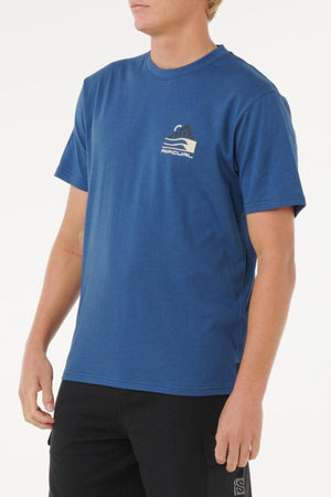 A person wearing a Rip Curl Vaporcool Search Range Tee in blue, featuring short sleeves and a small chest logo, stands against a plain white background.