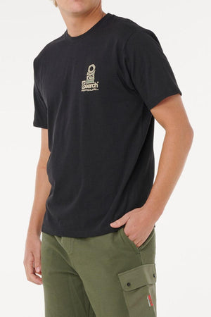 Someone wearing a black Rip Curl Vaporcool Search Stack Tee, featuring a small beige chest graphic, moisture control, and quick drying, paired with olive green cargo pants, stands with one hand in their pocket against a plain white background.
