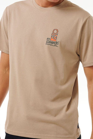 A person wears the Rip Curl Vaporcool Search Stack Tee, a beige relaxed-fit short-sleeved shirt with a small multicolored "Search Rip Curl" logo on the left chest. The person's head is not visible in the image.