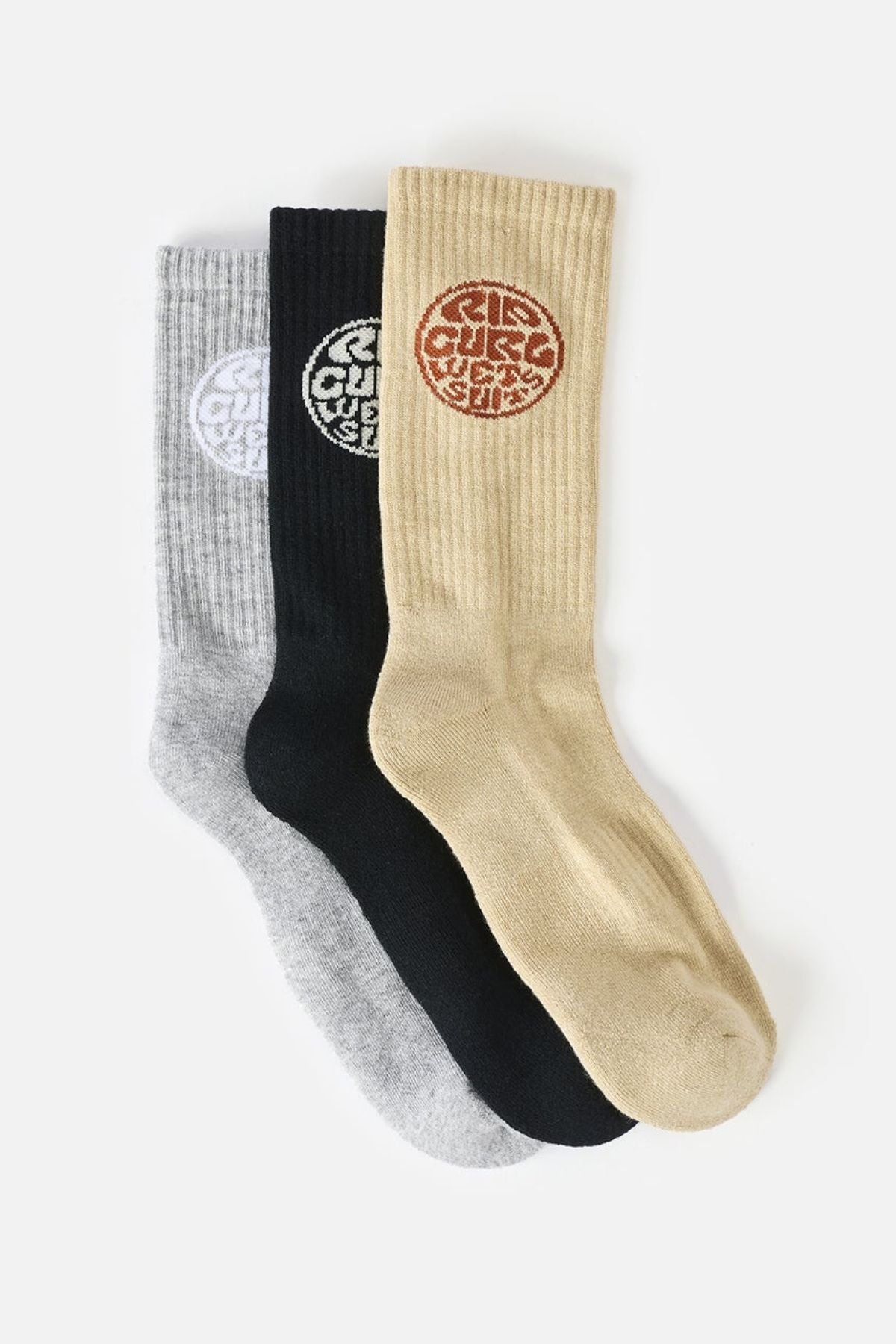 Three pairs from the Rip Curl Wetty Crew Sock 3 Pack in gray, black, and beige, each with a circular emblem featuring stylized text on the calf, are arranged overlapping on a white background. Crafted with moisture-wicking fabric and built-in arch support for all-day comfort.