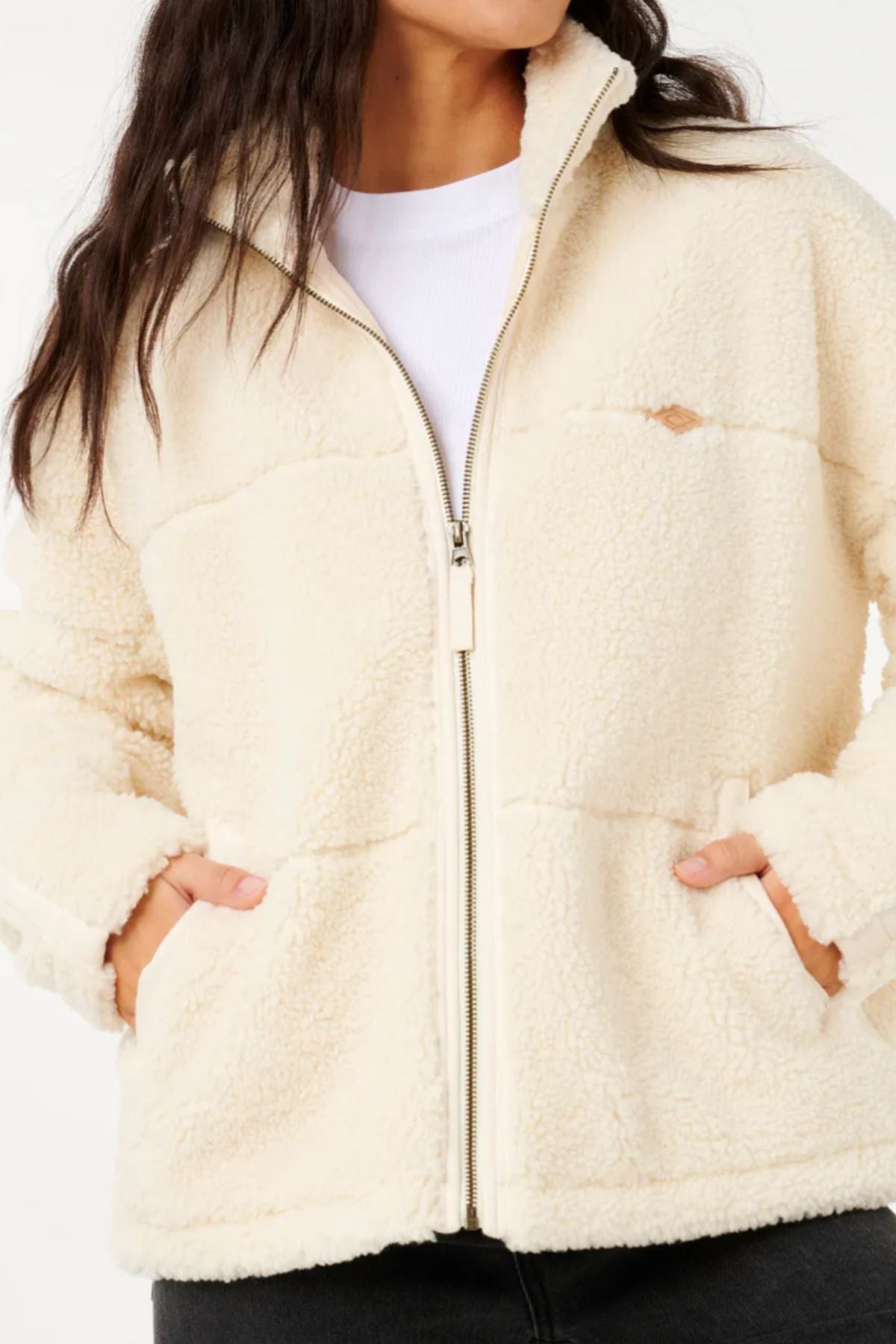 A person wears the cream Rip Curl Cala Nights Sherpa Jacket with their hands in the side pockets. Featuring a zip-up front and high collar, this cozy recycled polyester sherpa is a winter essential. The face is partially out of frame.