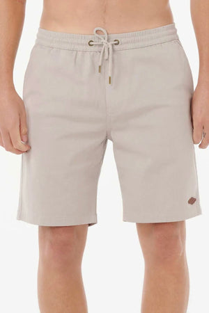 A person wears Rip Curl Classic Surf Volley shorts in light beige, featuring stretch cotton twill, elastic waistband with adjustable drawcord, and a small stitched logo on the lower left leg, standing against a white background.