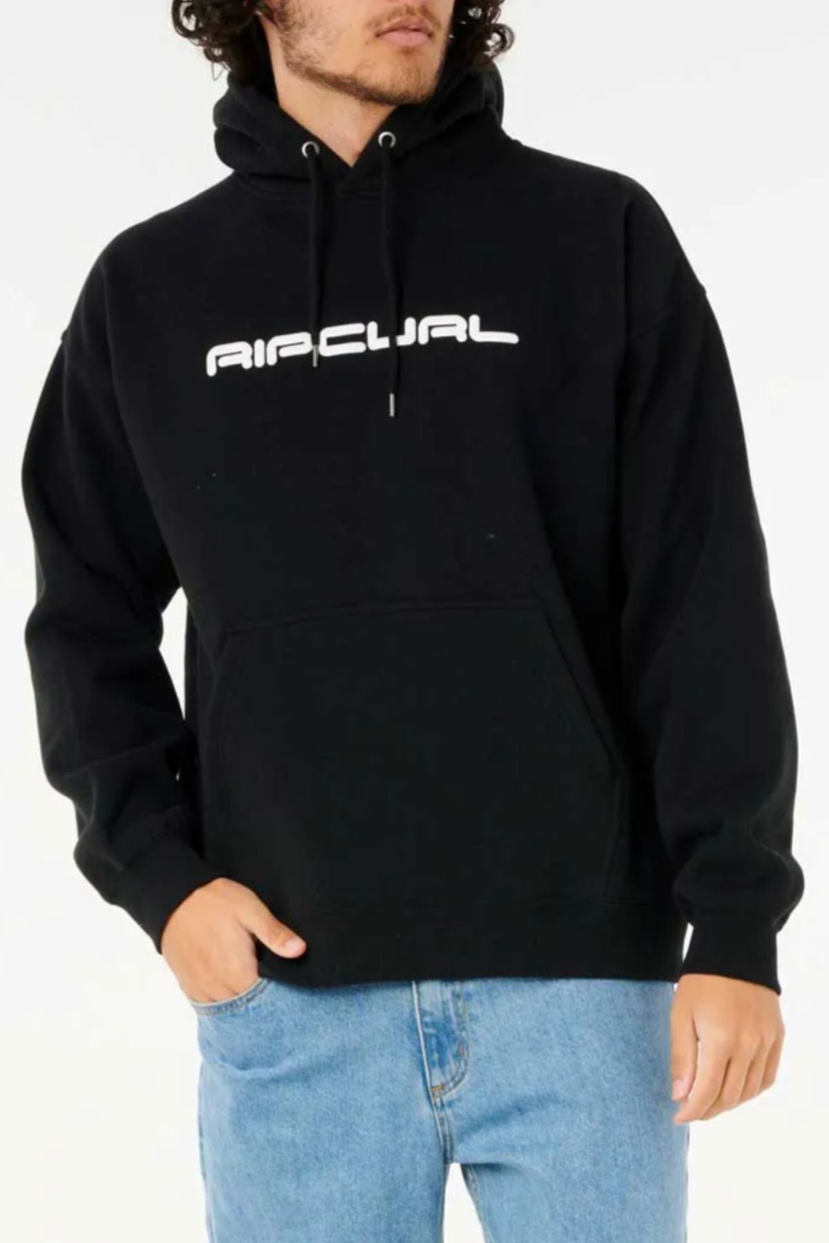 A person wearing a black Rip Curl Dosed Up Hood—crafted from soft cotton polyester fleece with "RIP CURL" in white on the chest—paired with light blue jeans, standing with one hand in the front pocket.