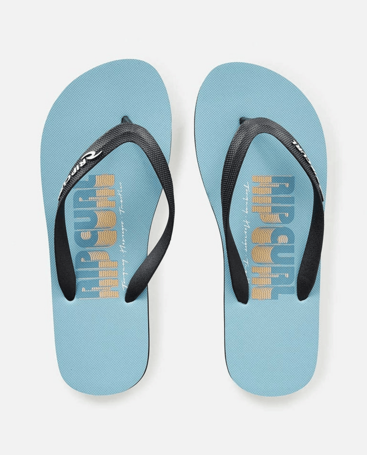 A pair of Rip Curl Surf Repeater Bloom Thongs in light blue, featuring ergonomic molded straps. "Rip Curl" and "Trippin’ Into Summer" are printed in blue and yellow on the footbeds.