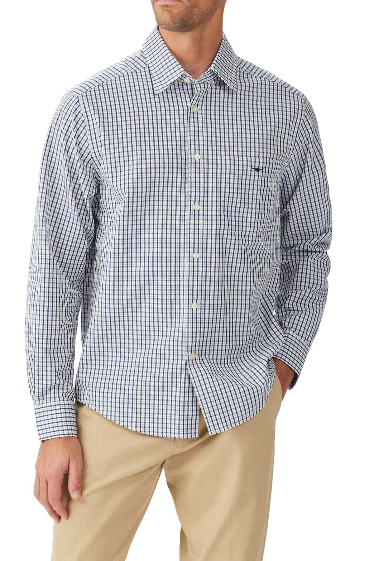 A man wearing the RM Williams Augusta Classic Poplin Shirt in blue and white checks and beige pants, standing with one hand in his pocket.