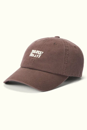 The RM Williams Branded Twill Cap is brown, made from organic cotton, and features a curved brim with white "DON'T TRIP." embroidery on the front and an adjustable strap. It is shown against a light background.