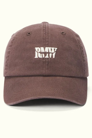 The RM Williams Branded Twill Cap is a brown organic cotton cap with a white embroidered “PMTW” heritage logo on the front, an adjustable strap, and is shown against a light background.