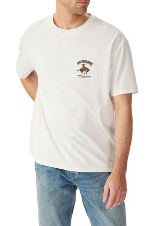 A man stands with one arm behind his back against a white background, wearing blue jeans and the RM Williams Cloudbuster T-Shirt—an organic cotton jersey tee in plain white with a small Cloudbuster motif and text on the chest.