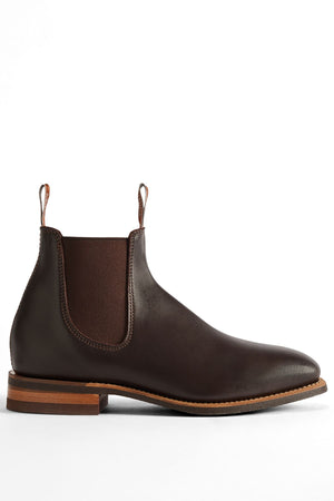 The RM Williams Comfort Craftsman Boot is a dark brown pull-up leather Chelsea boot with a low wooden heel, elastic side panels, and front and back pull tabs, shown in profile on a white background.