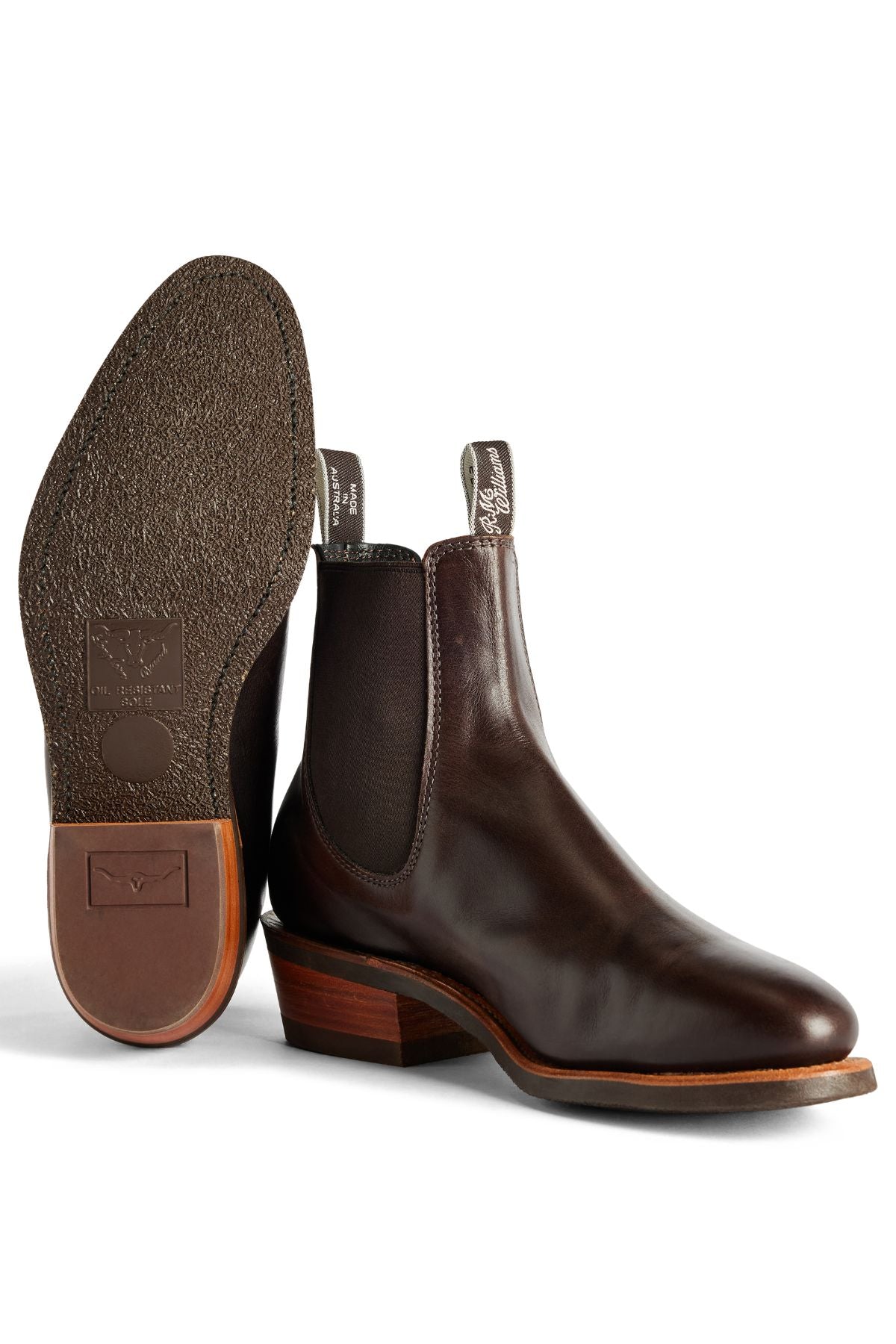 The RM Williams Comfort Lady Yearling Rubber Sole Boot in dark brown leather features elastic side panels, pull tabs, a textured sole, and a stacked wooden block heel. Shown with one boot upright and the other on its side. Made in Australia.
