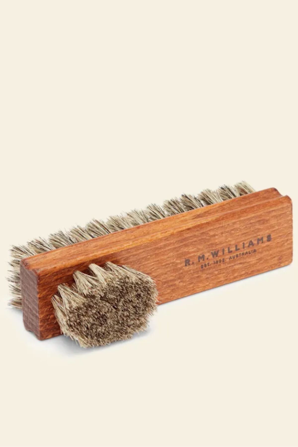 The RM Williams Double Sided Brush features a rectangular and a smaller oval-shaped wooden brush with natural bristles, ideal for cleaning or polishing full grain leather R.M.Williams boots.
