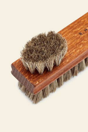 A close-up of the RM Williams Double Sided Brush with dense natural bristles on a light beige background. The smaller brush rests atop the larger, ideal for cleaning and polishing boots or full grain leather shoes.