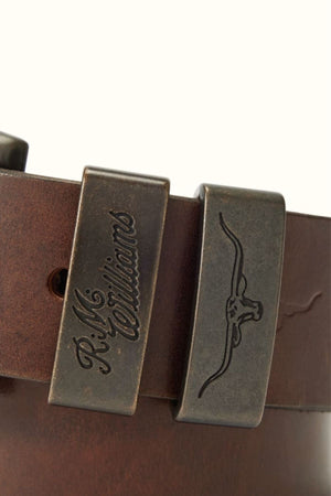 Close-up of the RM Williams Drover Belt in brown leather, featuring double keepers—one engraved with "R.M. Williams" and the other displaying a longhorn cattle head design.