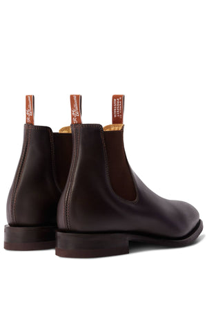 The RM Williams Dynamic Flex Craftsman Boot is shown at an angle, displaying its handcrafted dark brown yearling leather, brown elastic side panels, visible stitching, and branded pull tabs.