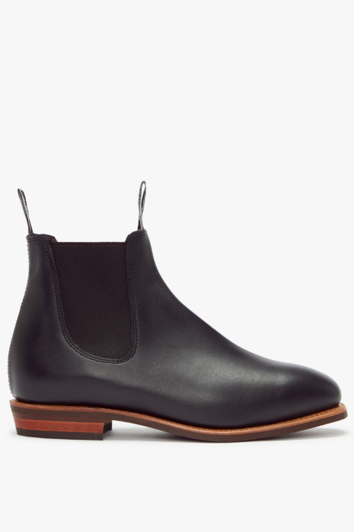 The RM Williams Erica Boot is a black full-grain leather Chelsea boot featuring elastic side panels, pull tabs, and a brown stacked heel, shown against a white background.