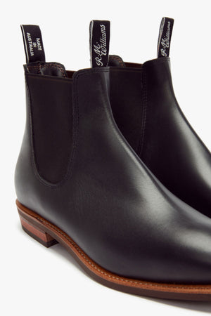 The RM Williams Erica Boot is a black full-grain leather Chelsea boot with elastic side panels, white-text pull tabs, and brown soles with a slight heel—crafted in the signature Craftsman style.