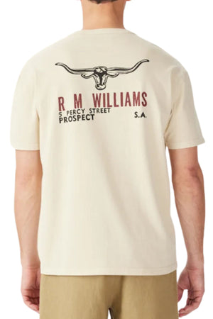 A person wears the RM Williams Flinders T-Shirt, a relaxed fit, cream organic cotton jersey featuring a Longhorn print and "R M Williams, 5 Percy Street, Prospect, S.A." on the back in black and red.