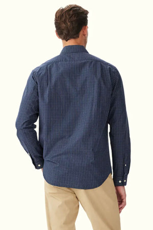 A man is shown from the back wearing the RM Williams Kimberley Regular Poplin Shirt in navy blue checkered pattern with buttoned cuffs and a curved hem, paired with beige pants against a plain light-colored background.