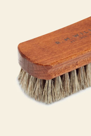 A close-up of the RM Williams Medium Brush, featuring dense horse hair bristles and a smooth, rounded wooden body. Set against a plain light background.