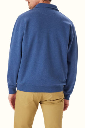 A man is shown from the back wearing the RM Williams Mulyungarie Fleece, a blue quarter zip sweater made of organic cotton, with tan pants, standing against a plain light background.